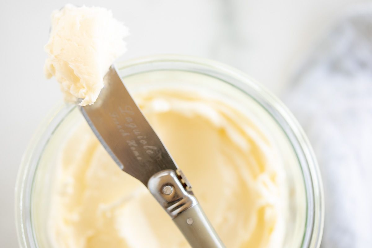 A knife placed over a small glass bowl of homemade butter