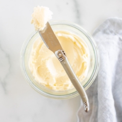 A knife placed over a small glass bowl of homemade butter