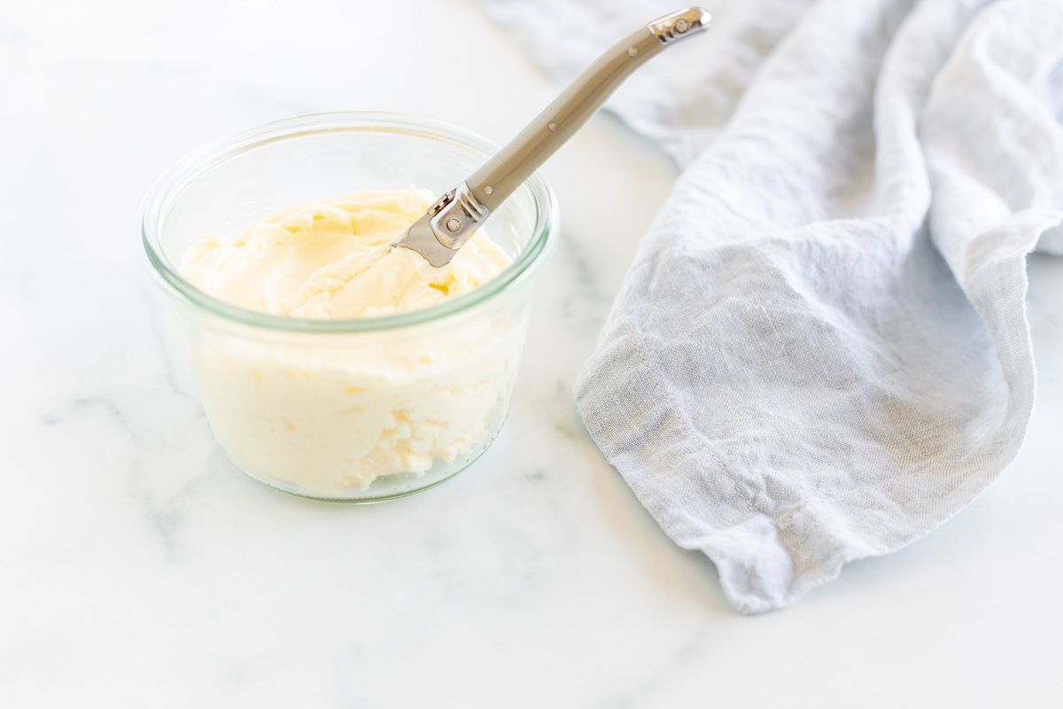 A knife placed over a small glass bowl of homemade butter