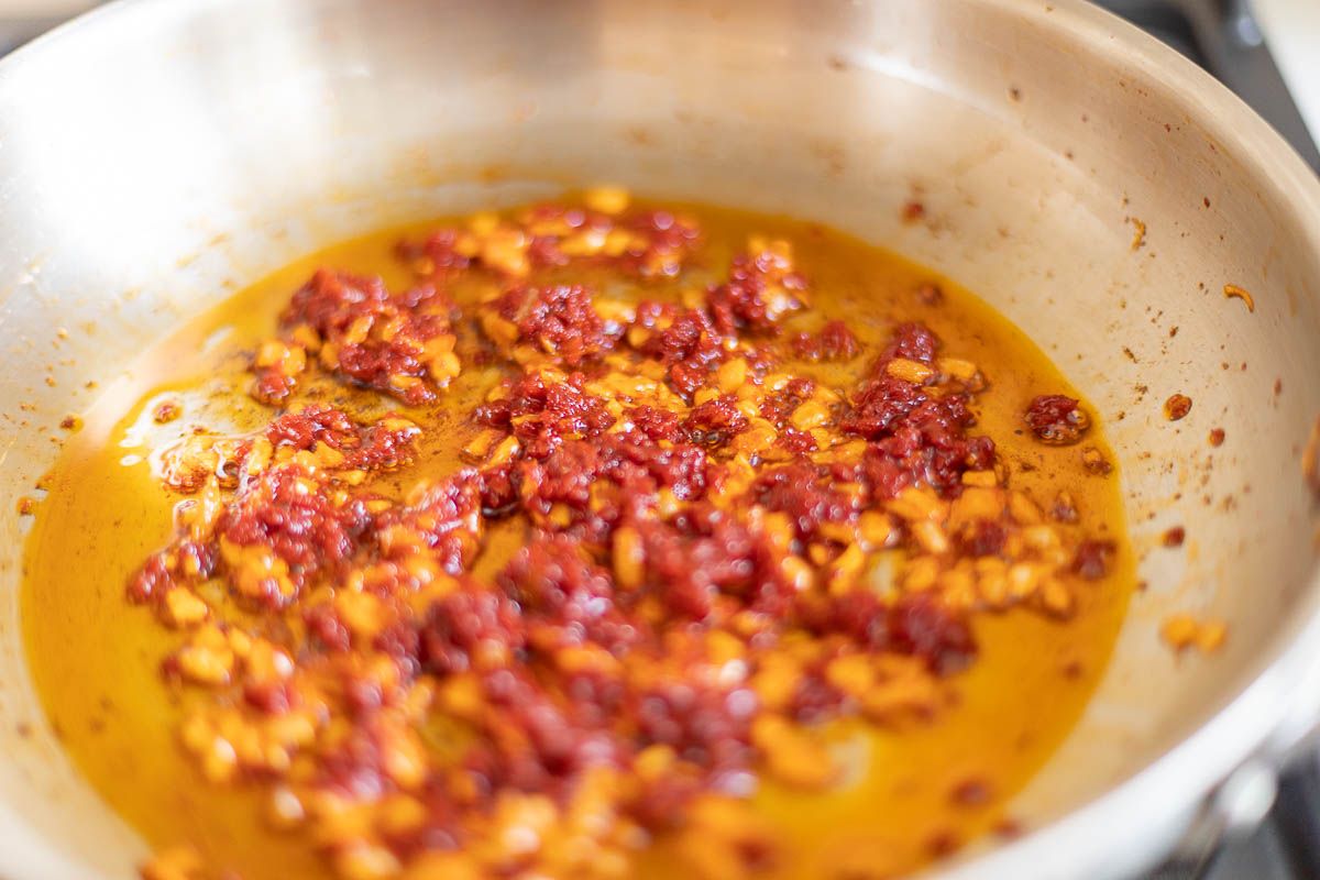 A silver pan with garlic and shallots and tomato paste.