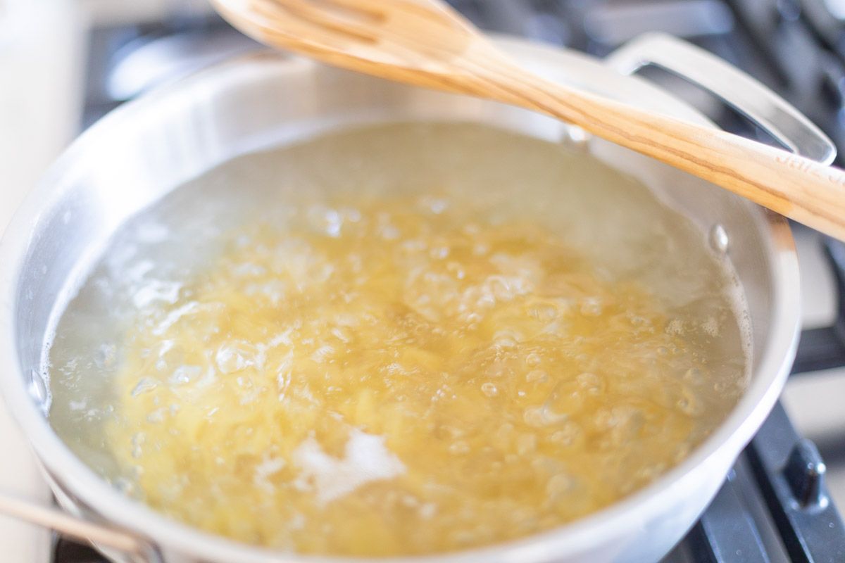 Shell pasta cooking in a silver pot of boiling water, wooden spoon resting across the top.