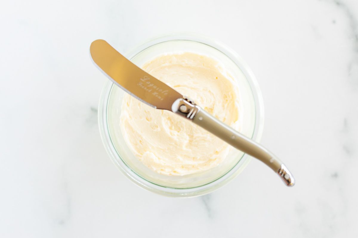 A knife placed over a small glass bowl of homemade butter