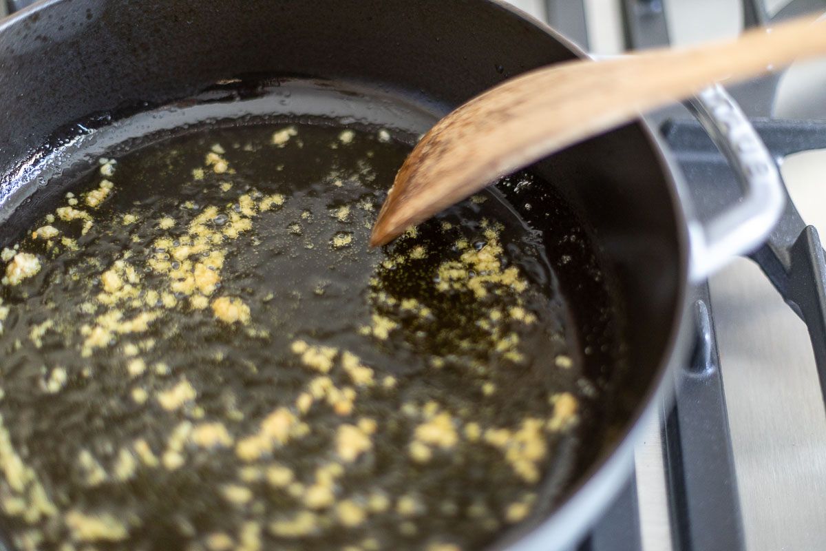Garlic in a saute pan, with a wooden spoon pushing it around