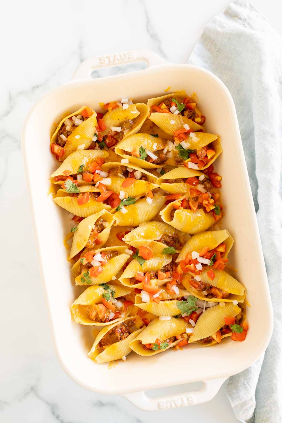 Taco stuffed shells in a white baking pan.