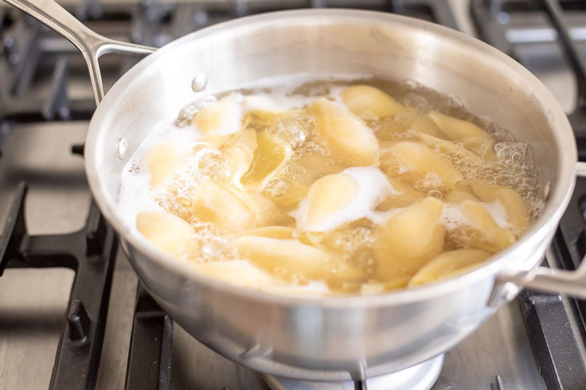 A pan full of jumbo shells cooking in boiling water on a stovetop