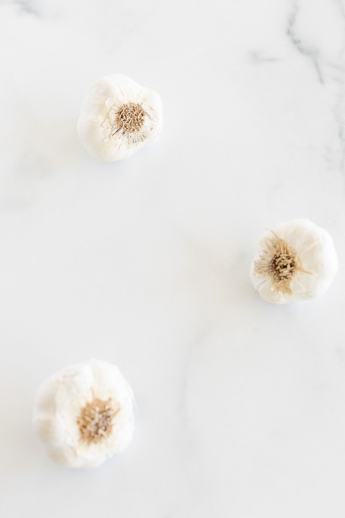 Three garlic bulbs laid out on a marble countertop