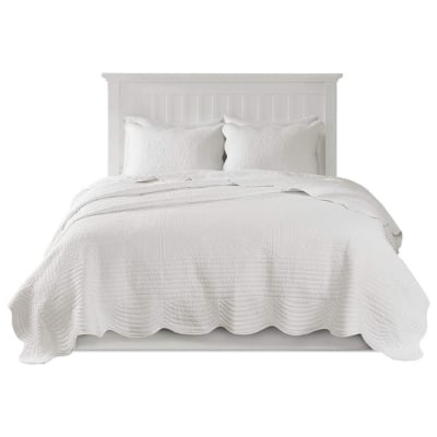 A white bed with scalloped white quilt