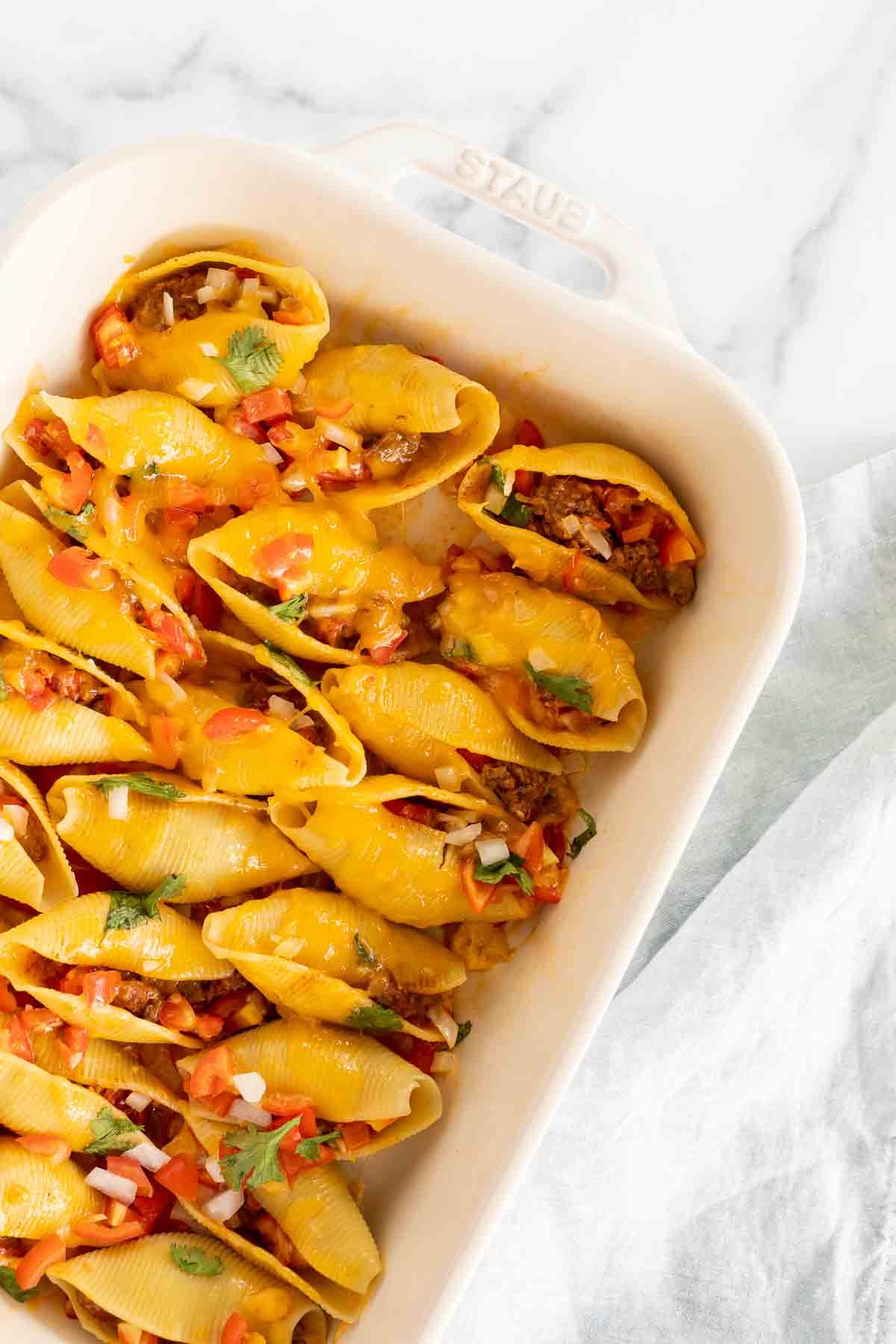 Taco stuffed shells in a white baking pan.
