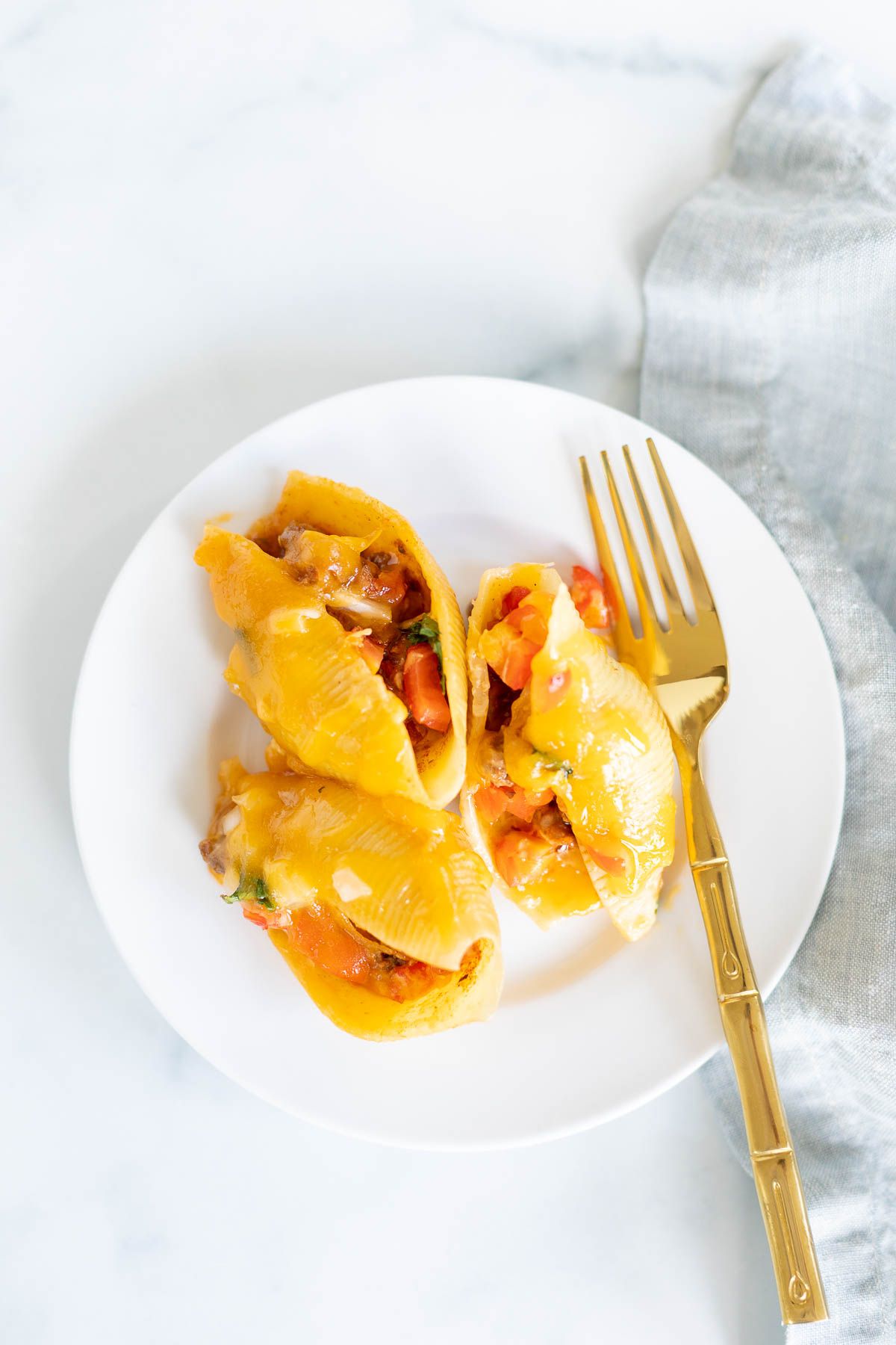 A serving of taco stuffed shells on a white plate with a gold fork.