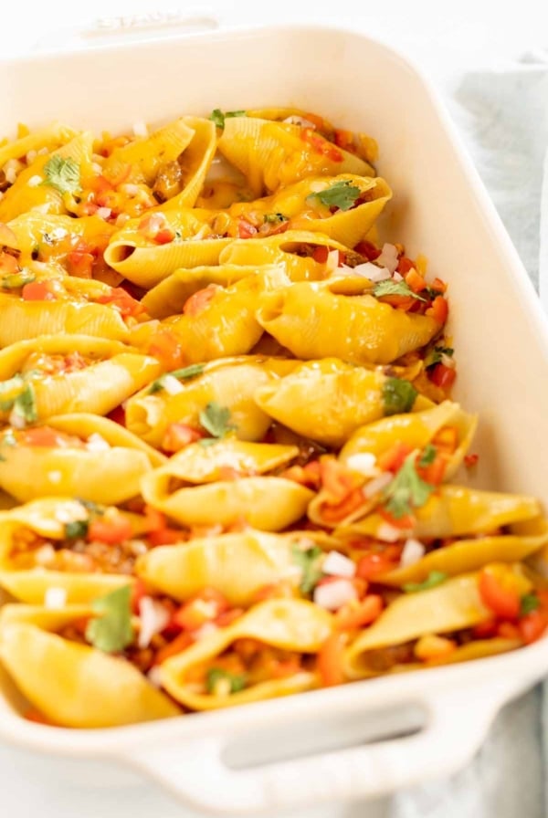 Taco stuffed shells in a white baking pan.