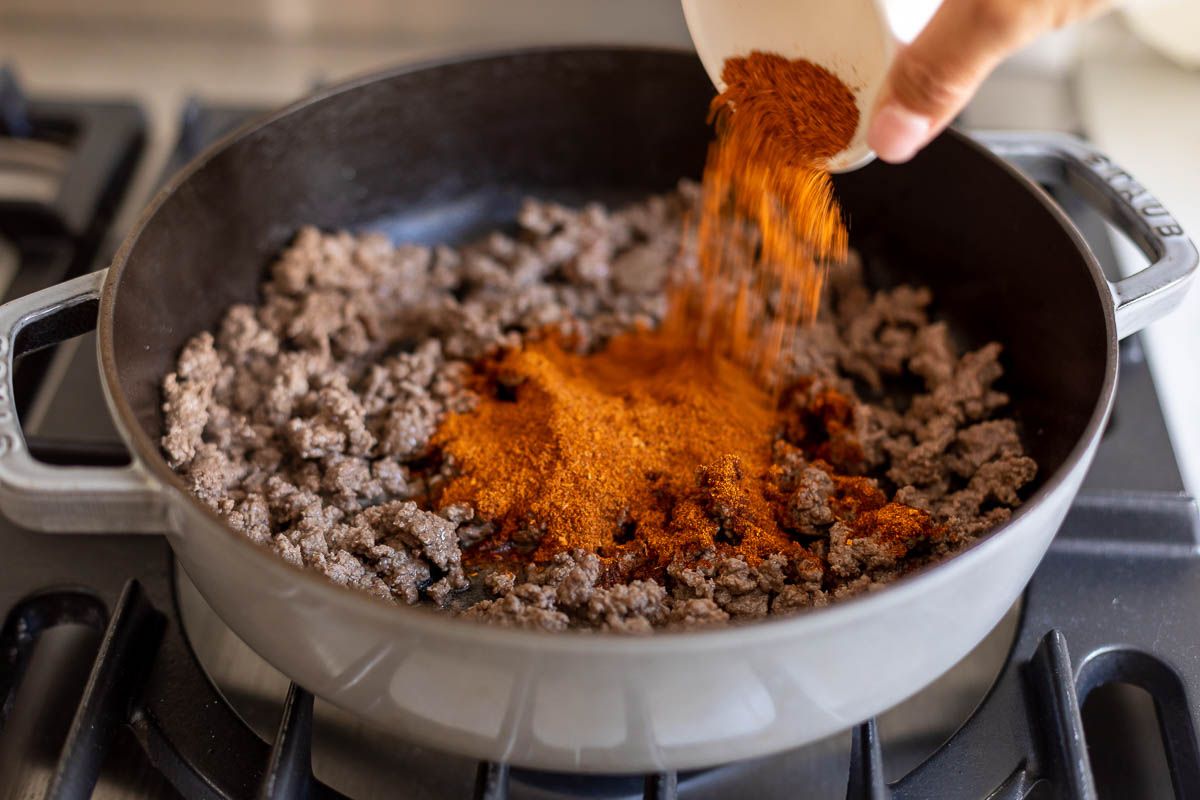 Taco seasoning added to a pan full of ground beef on a stovetop.