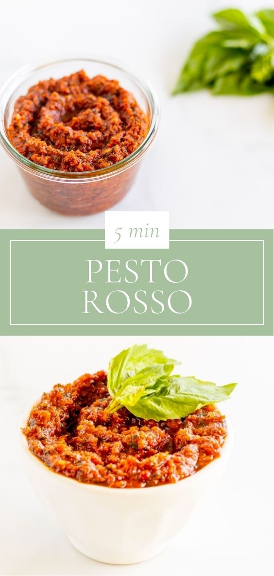 A small white bowl of pesto rosso, placed next to basil leaves, placed on a marble countertop.