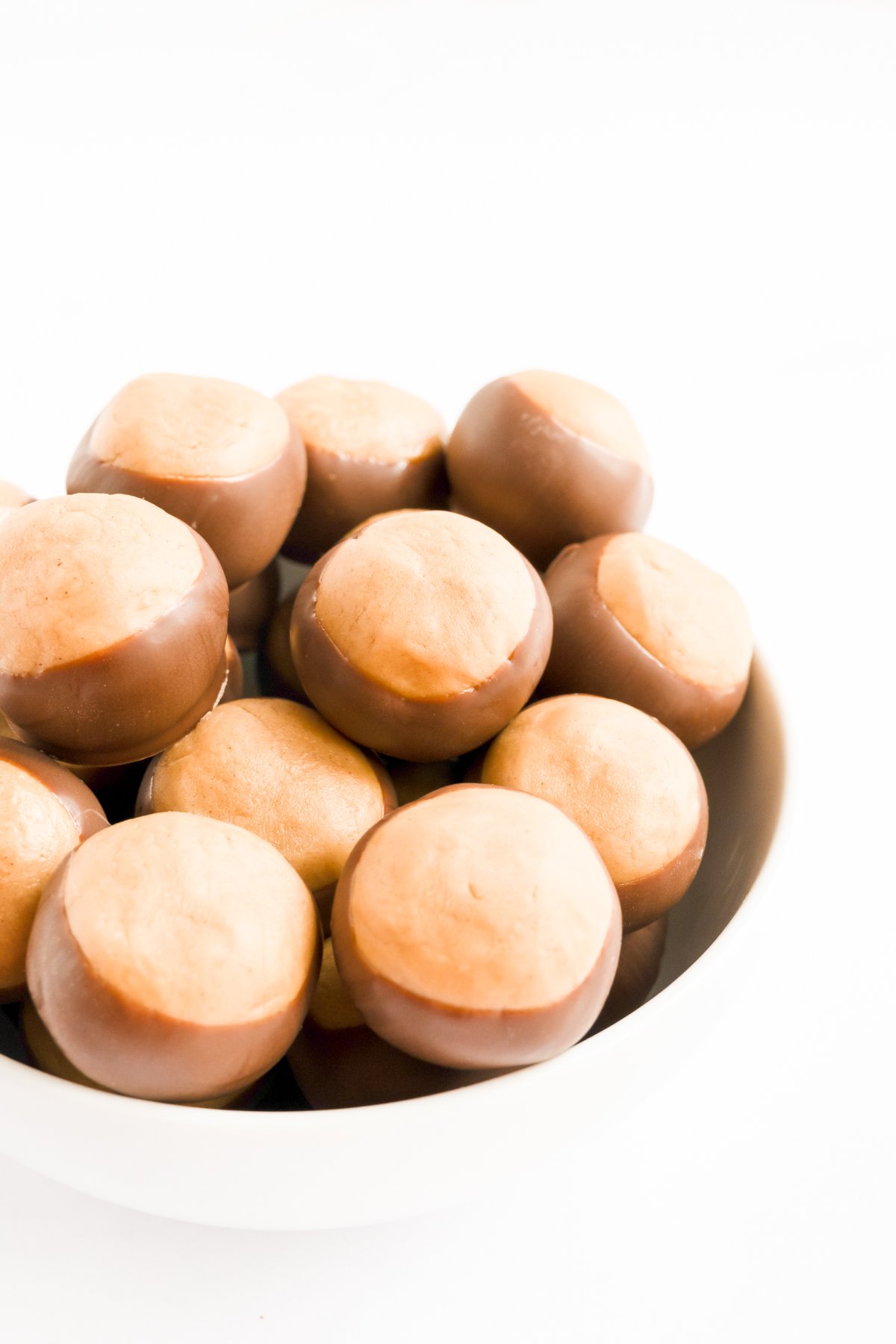 A bowl of chocolate covered peanuts, resembling a buckeye recipe, on a white surface.