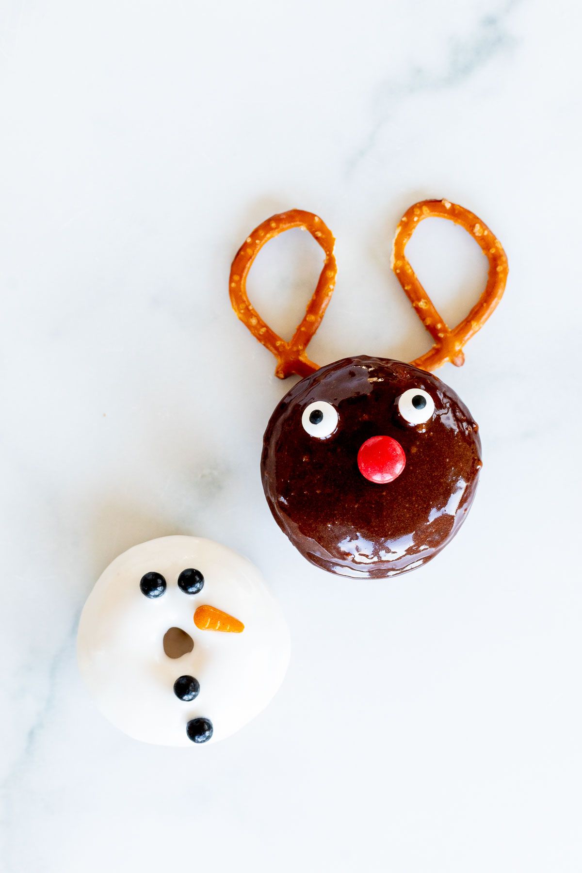 A reindeer donut and a snowman donut on a marble countertop.