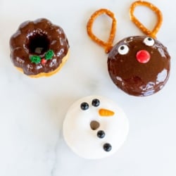 Three cute Christmas donuts on a marble countertop.