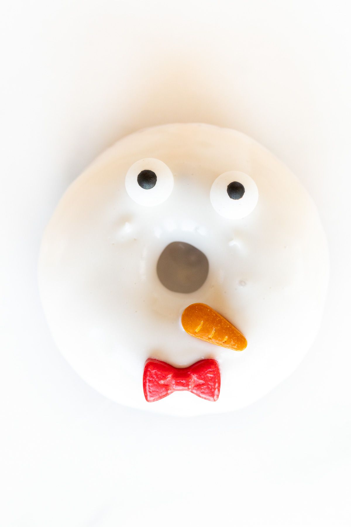 A white homemade snowman Christmas donut on a white surface.