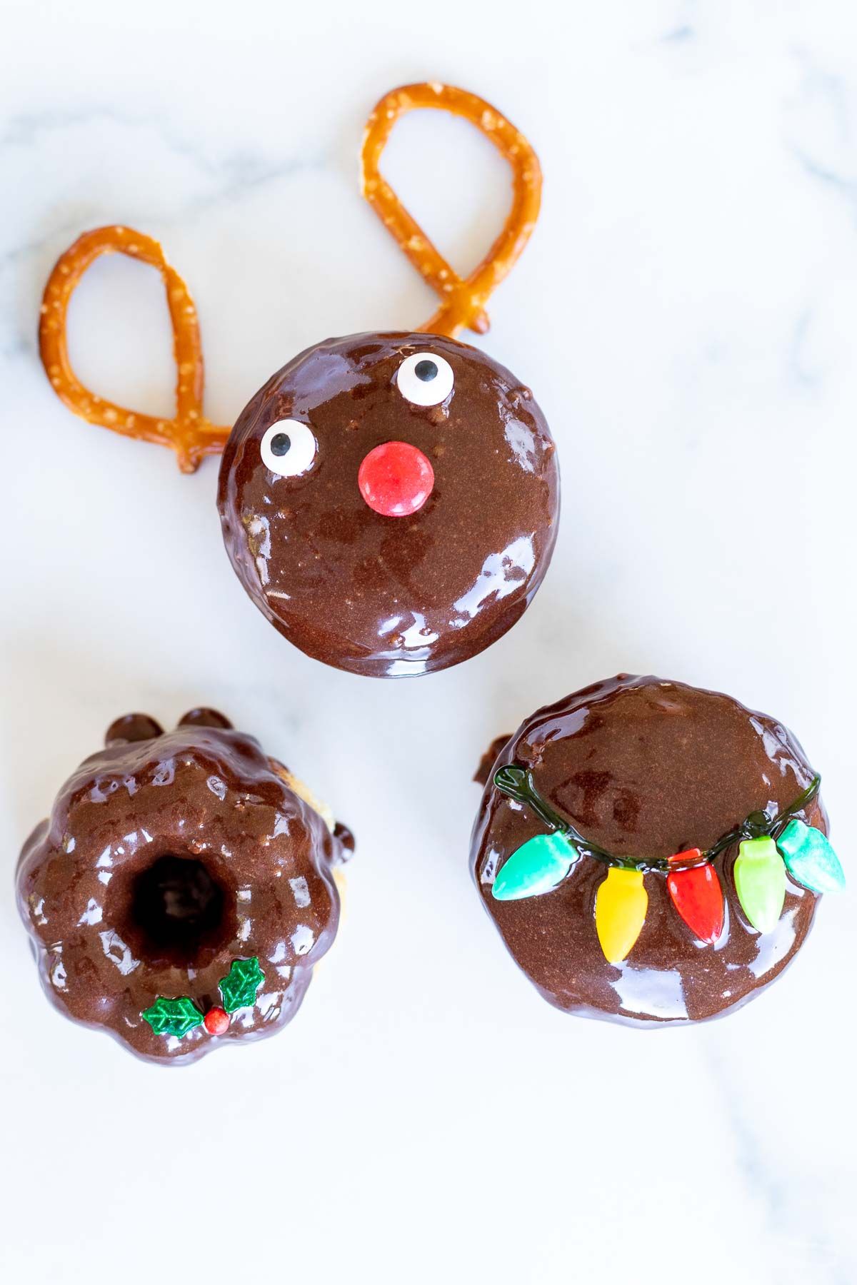 Three cute Christmas donuts on a marble countertop.