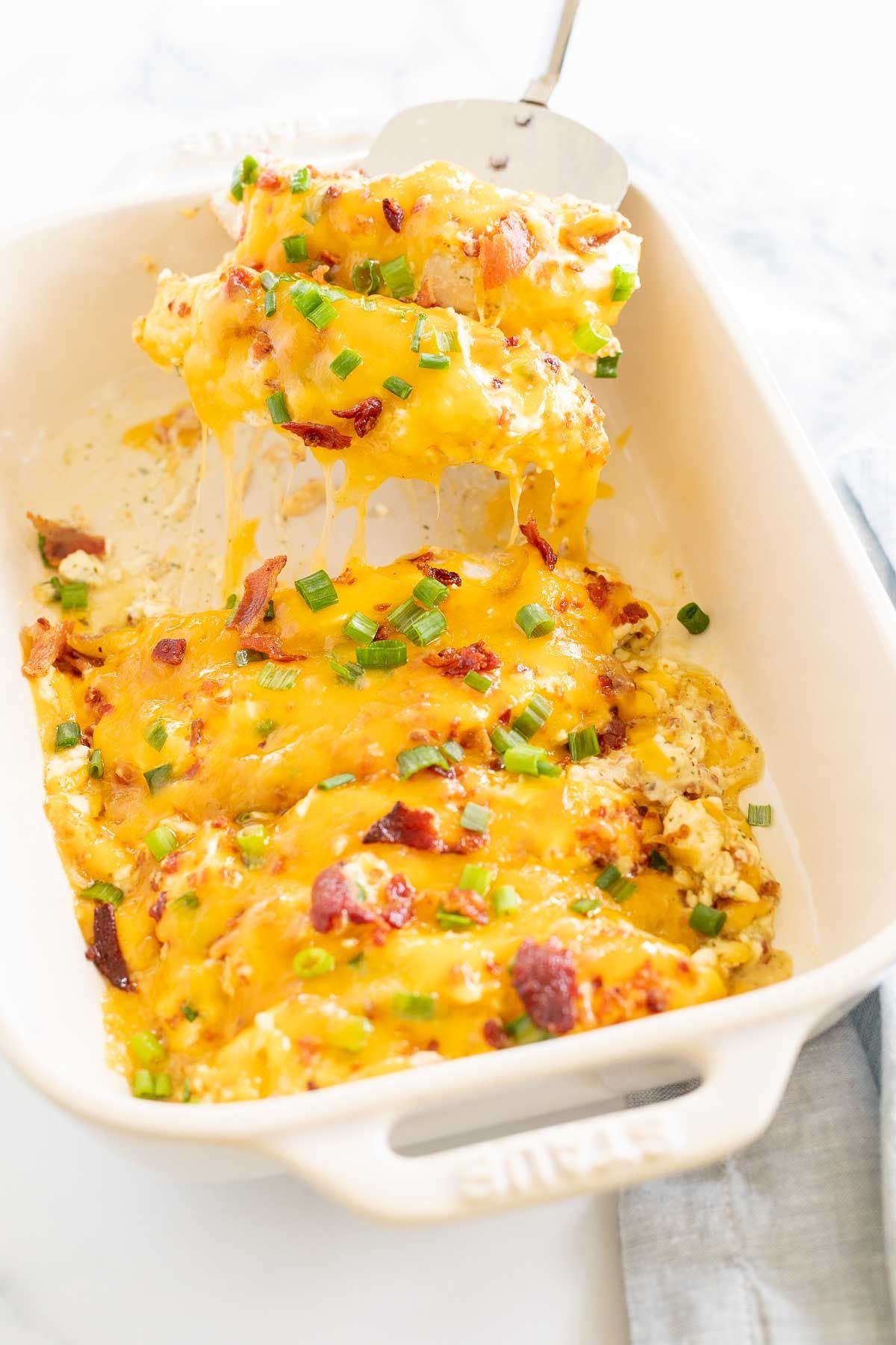 Baked crack chicken breasts in a white baking dish, with a silver spatula lifting a serving out.