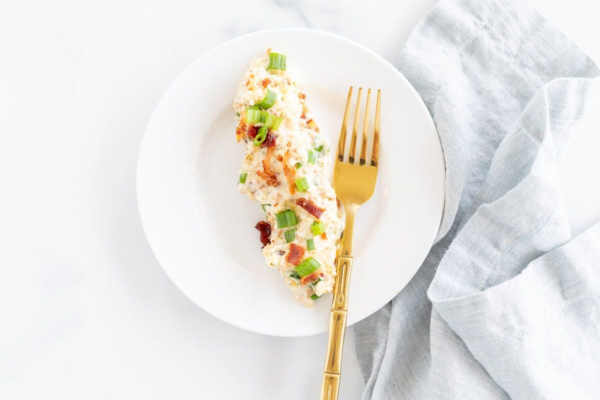 A crack chicken tenderloin serving on a white plate with a gold fork.