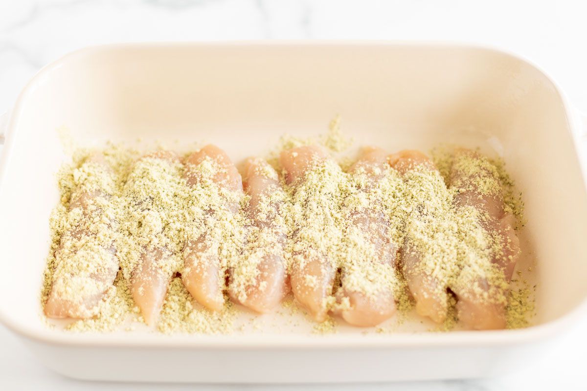 Chicken tenderloins topped with seasoning in a white baking dish, prior to baking.