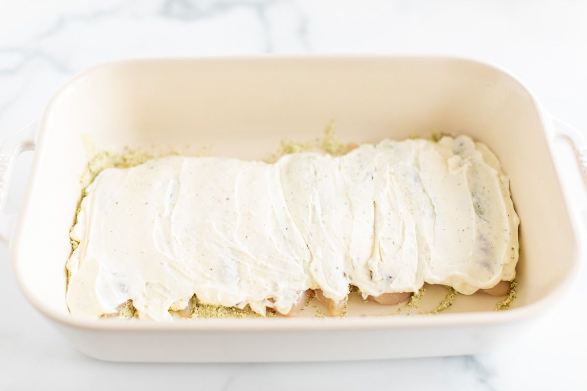 Chicken tenderloins topped with seasoning in a white baking dish, prior to baking.