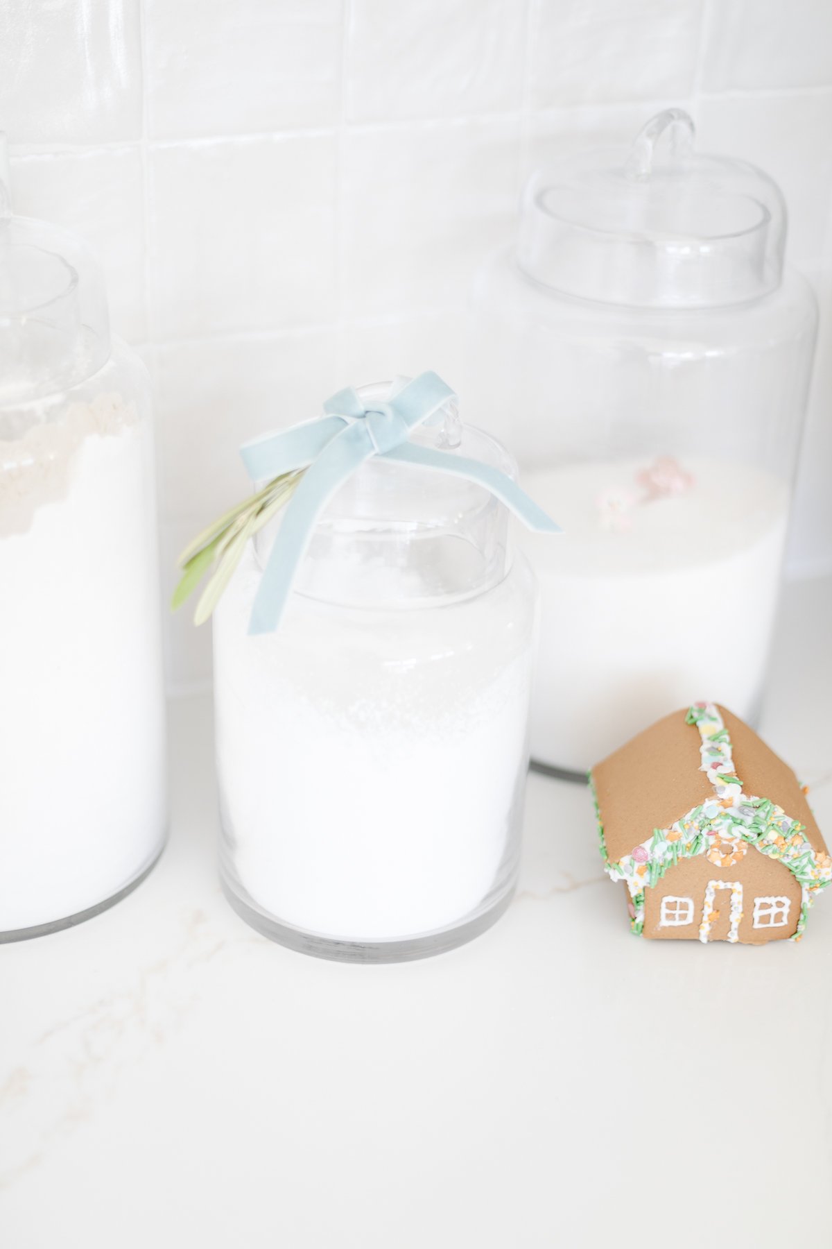 At a kitchen counter, you will find three jars of sugar and a gingerbread house.