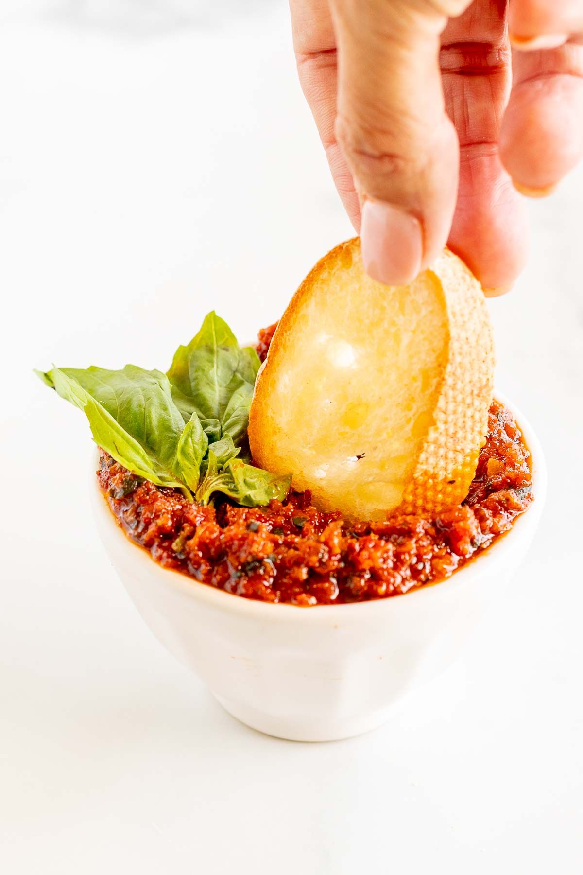 Hand dipping a slice of crostini into a bowl of pesto rosso.