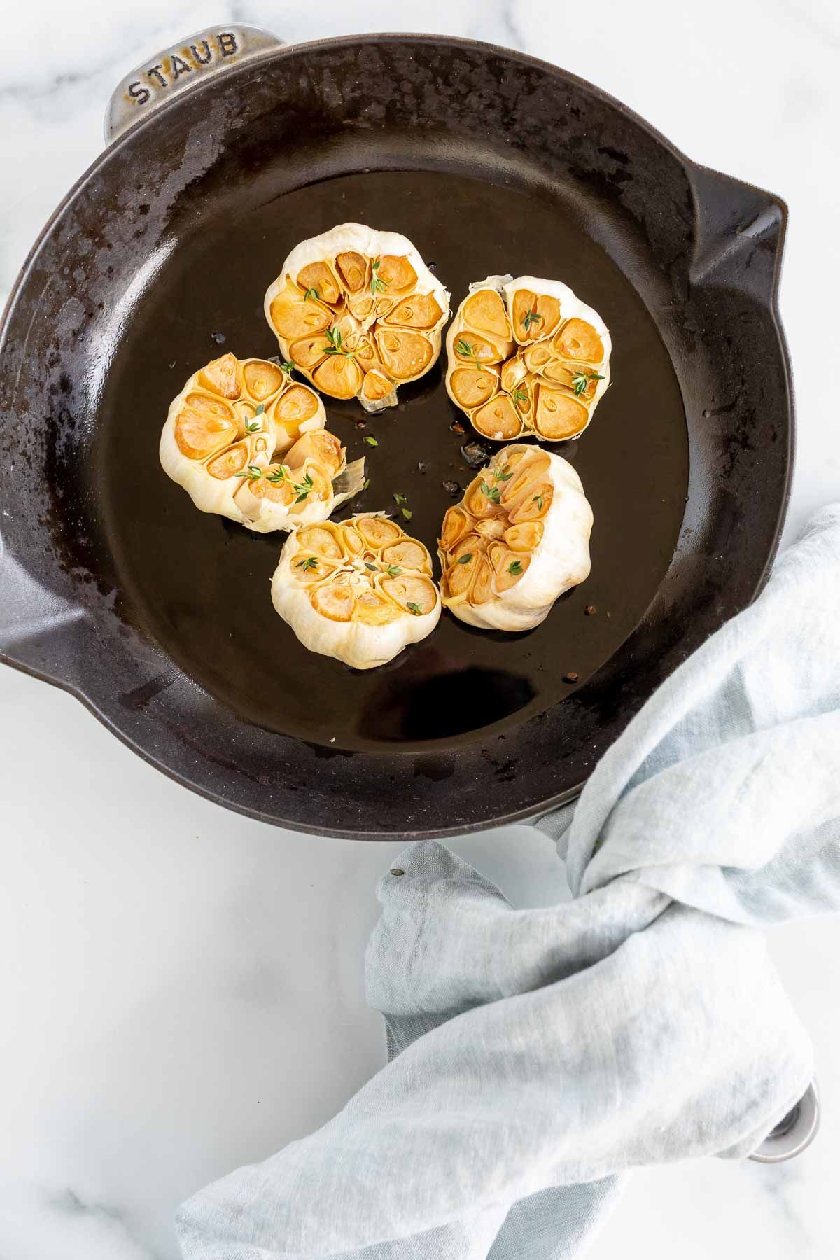 Five heads of roasted garlic in a cast iron pan.