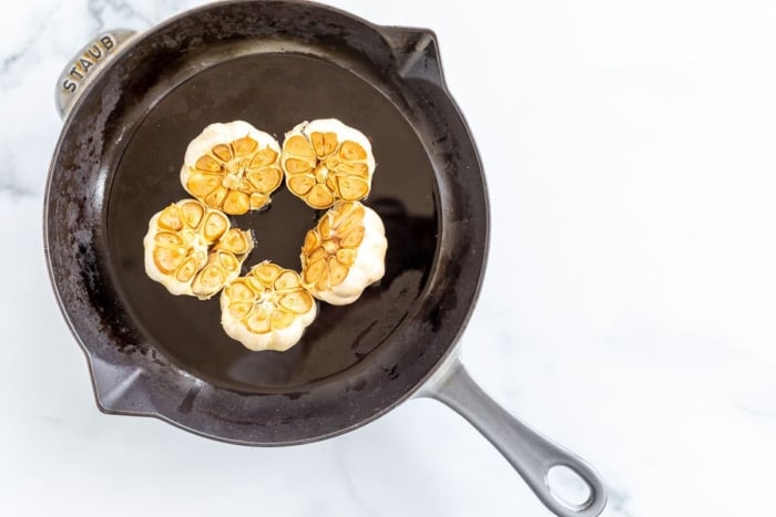 Five heads of roasted garlic in a cast iron pan.
