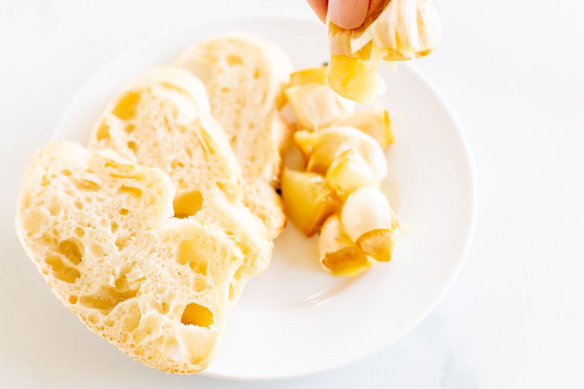 A white plate with sliced French bread and cloves of roasted garlic.