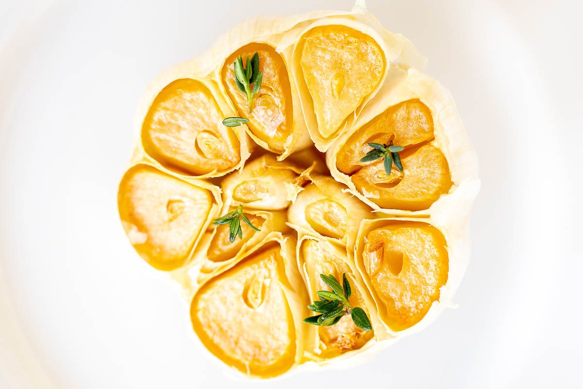 A close up of a roasted garlic head, garnished with fresh thyme leaves.