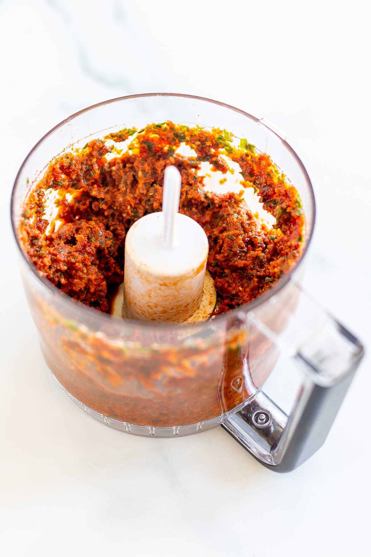 A food processor filled with ingredients for sun dried tomato pesto
