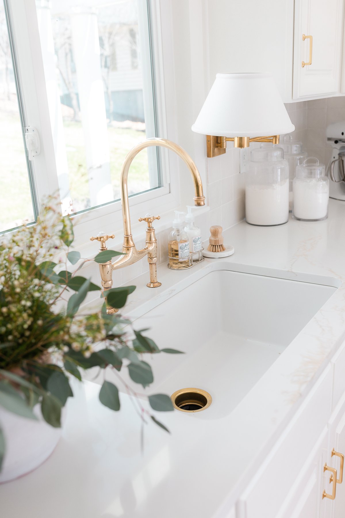 white kitchen with brass faucet, pulls and sconce