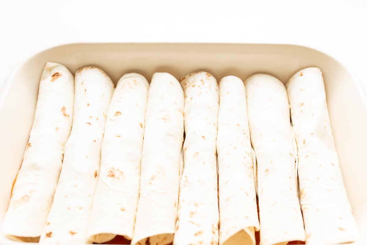 Cheese enchiladas in a white baking dish, before the sauce goes on.