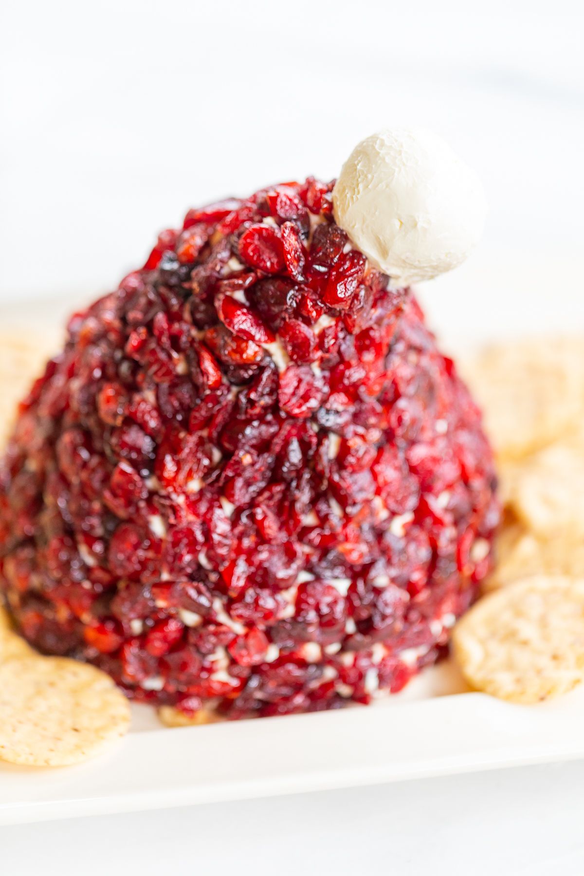 A cranberry cheeseball in the shape of a Santa's hat, on a plate surrounded by crackers.