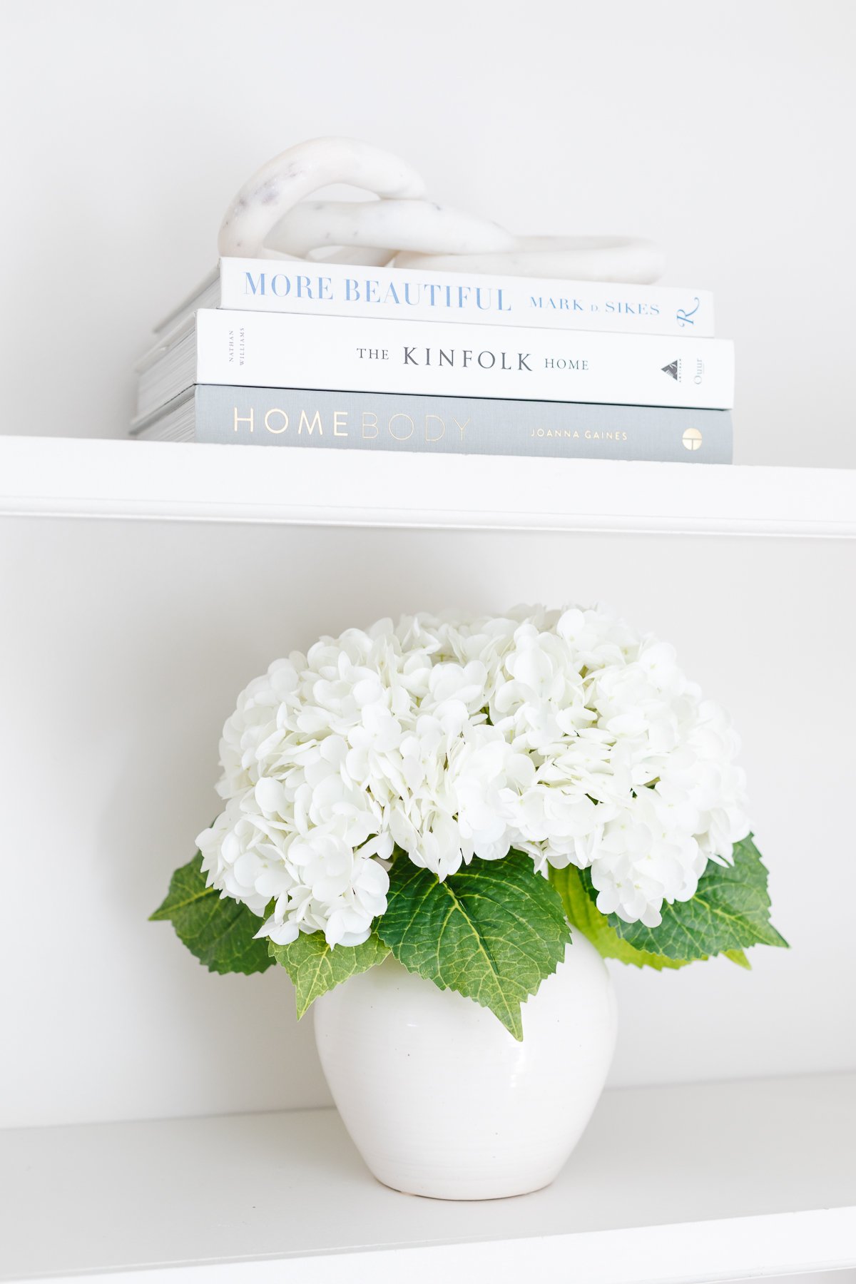 Decluttered white hydrangeas in a vase on a bookshelf.