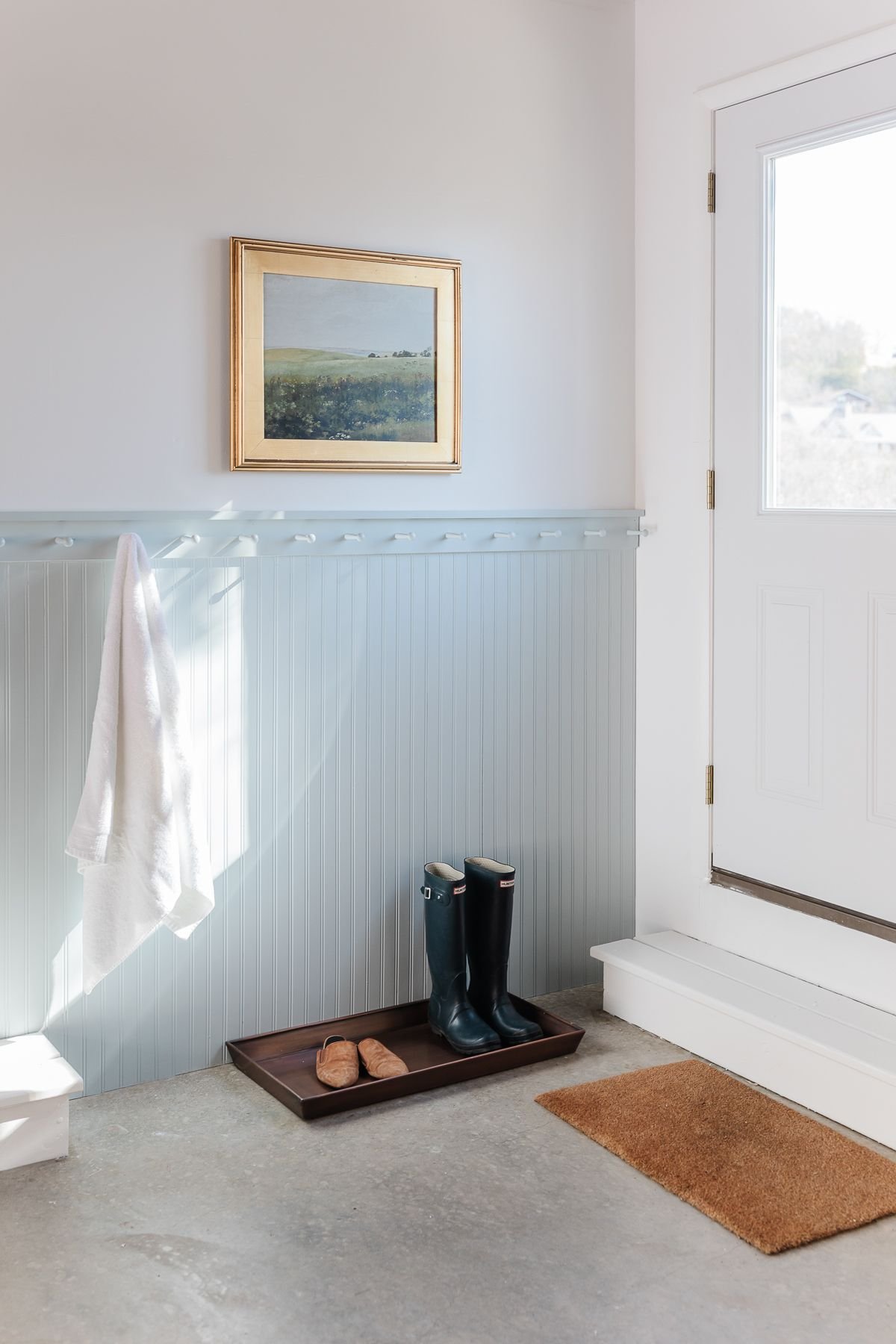 A blue painted mudroom area with a boot tray on the ground.
