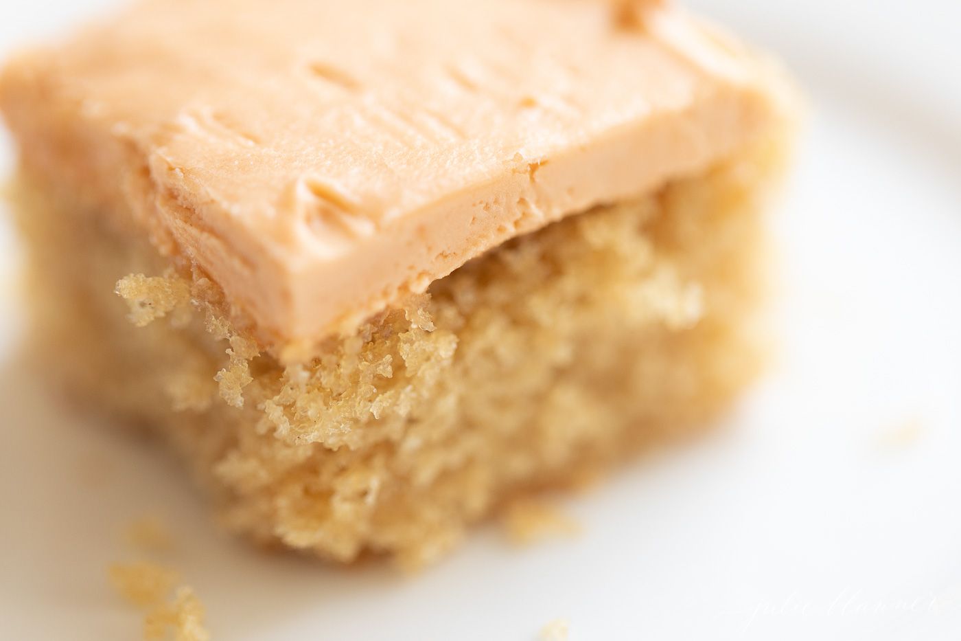 Slice of frosted butterscotch cake on a white plate, crumbs on plate.