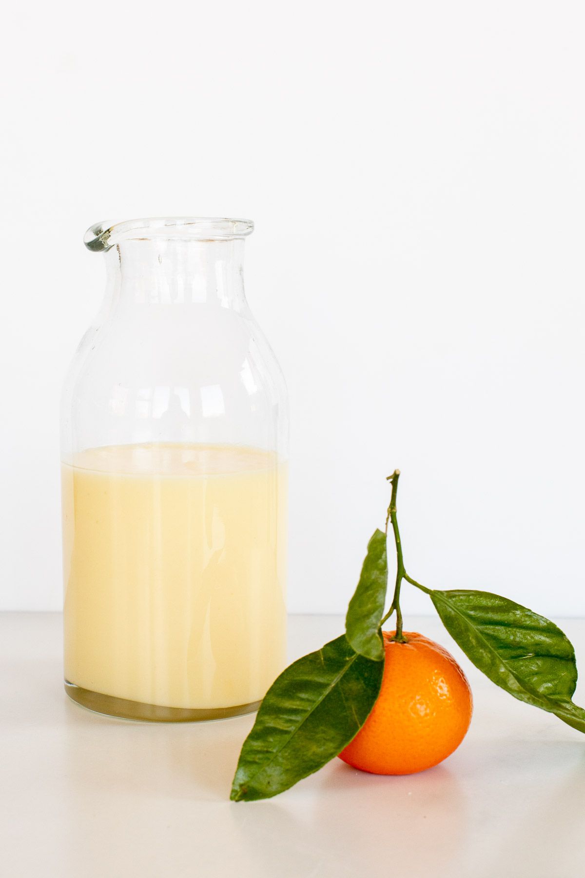 a glass jar of orange glaze frosting, with a small mandarin orange to the side. 