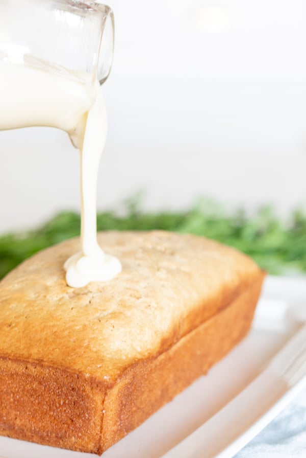 A loaf of bread with homemade frosting pouring over the top from a glass bottle.