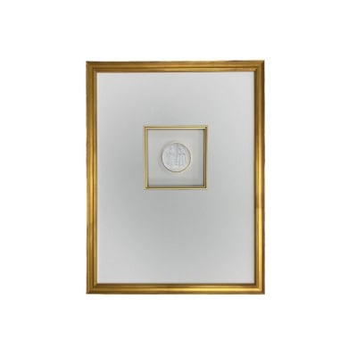 A framed, centered smaller frame within a larger golden frame, containing a white circular intaglio with an indistinguishable design. The background is plain white.