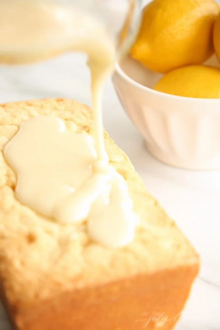 A homemade lemon glaze frosting pouring over a loaf of lemon pound cake. 
