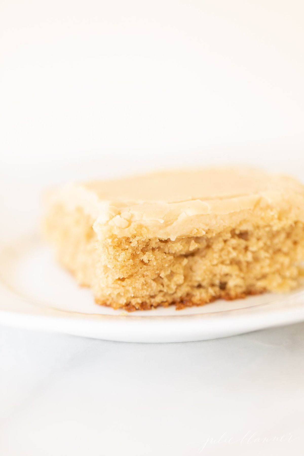 White surface with a white plate, slice of peanut butter cake with frosting.