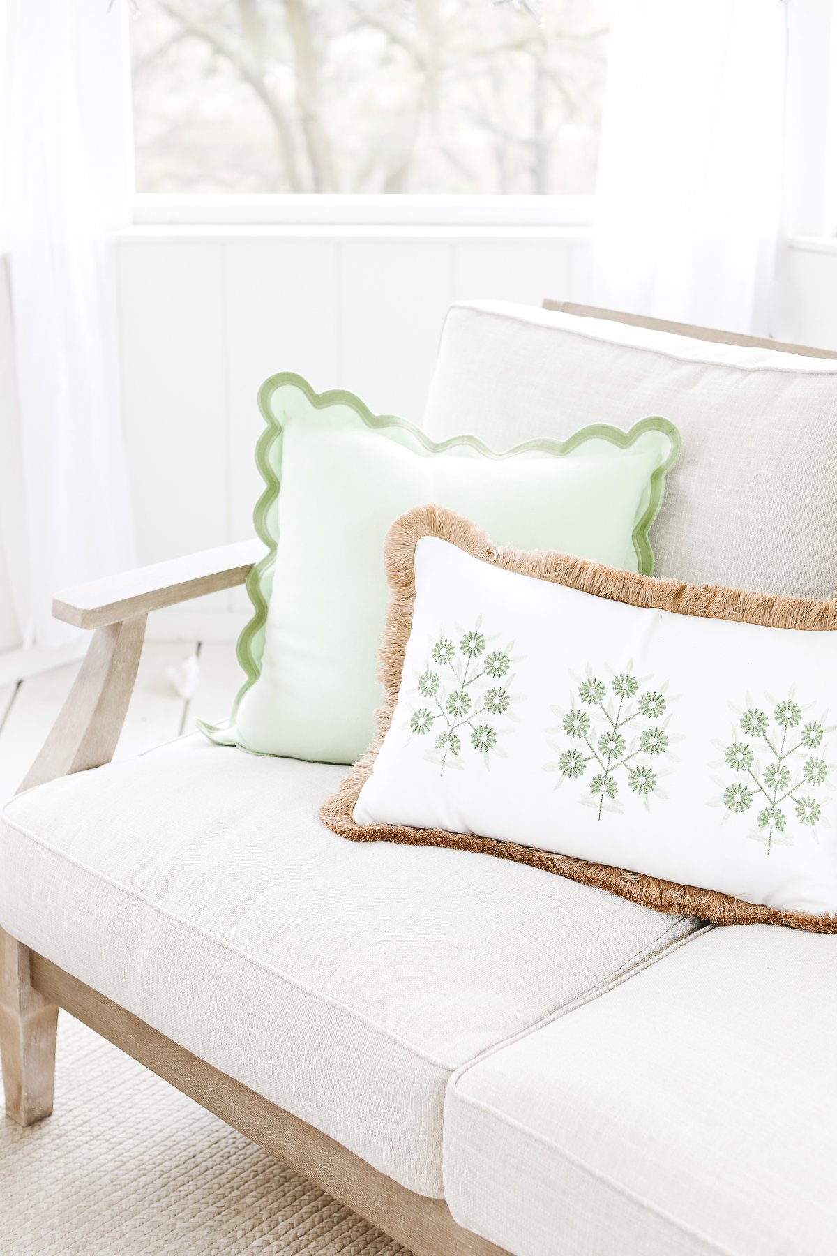 A white couch with a scalloped green pillow on it.