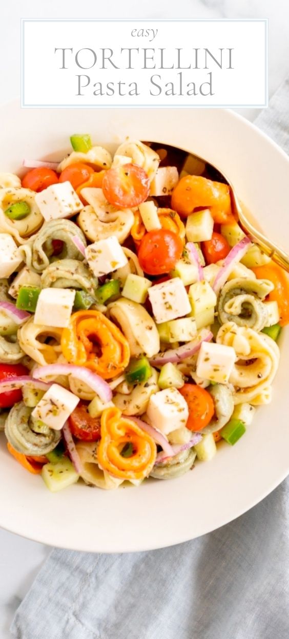 A white serving bowl full of tortellini pasta salad, gold serving spoon on the side.