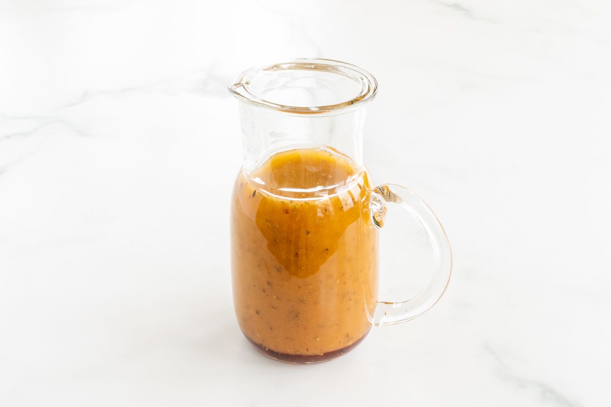 A small glass pitcher full of homemade Greek Salad dressing, on a white countertop.