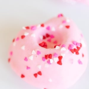 Heart shaped Valentine doughnuts on a white surface, covered in pink icing and sprinkles.