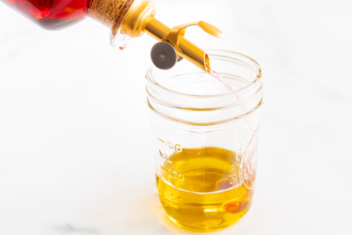 Ingredients for a Greek salad dressing recipe being added to a glass jar.