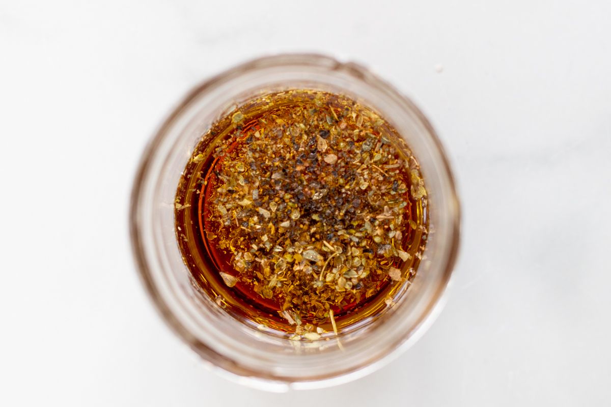 Ingredients for a Greek salad dressing recipe being added to a glass jar.