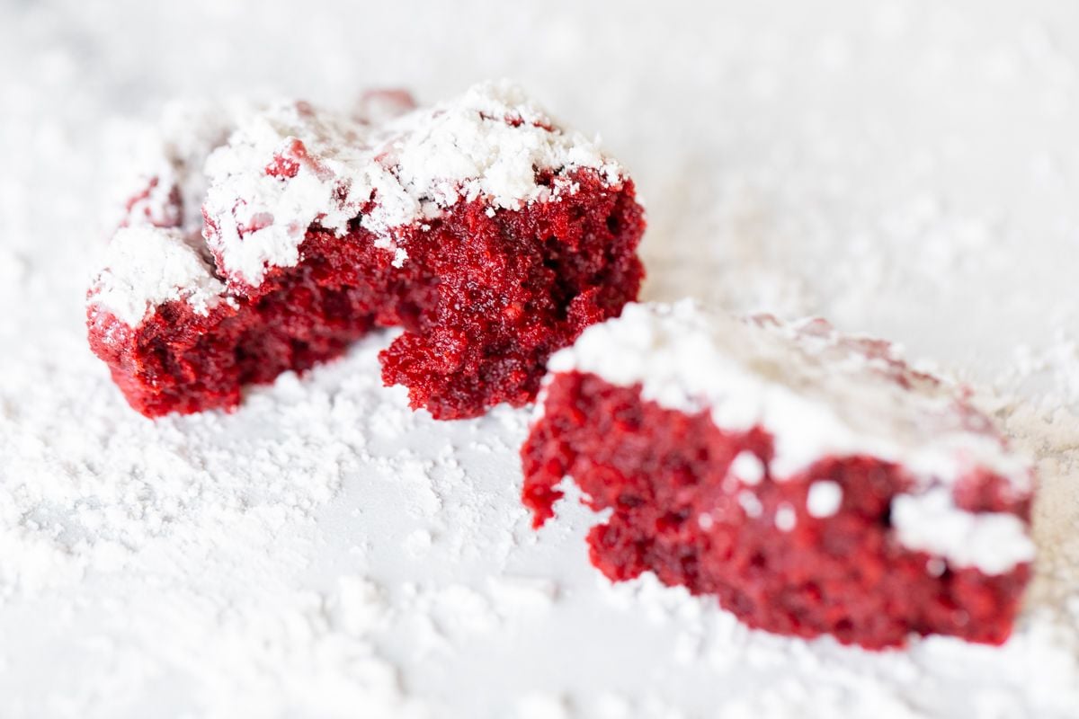 Red velvet gooey butter cookies dusted in powder sugar on a white countertop.